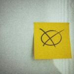 A yellow sticky note with a large black crossed circle on a white surface, perfect for business or office themes.